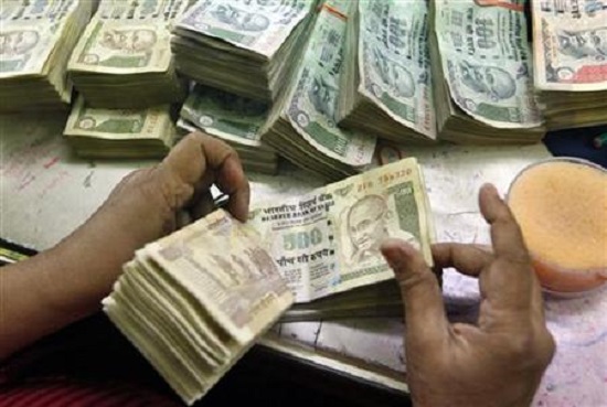 An employee counts Indian currency notes at a cash counter inside a bank
